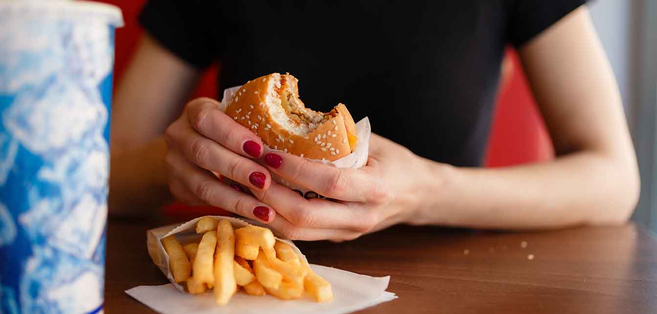 Woman eating a burger, french fries, and a soft drink